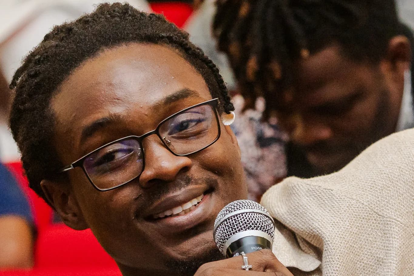 An attendee in glasses smiling as he asks a question into a microphone from the audience