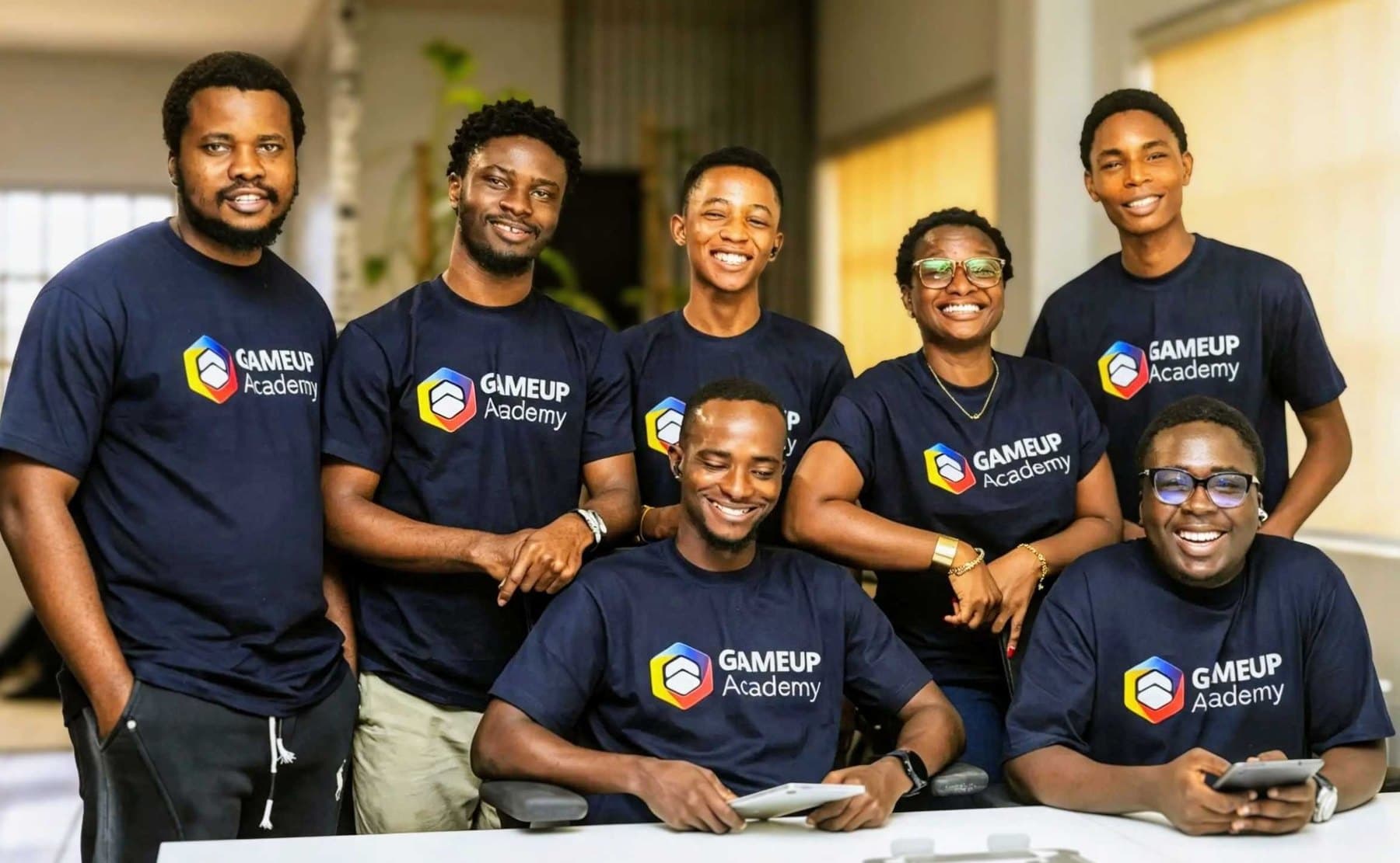 Seven smiling GameUp Academy team members in matching navy GameUp Academy t-shirts