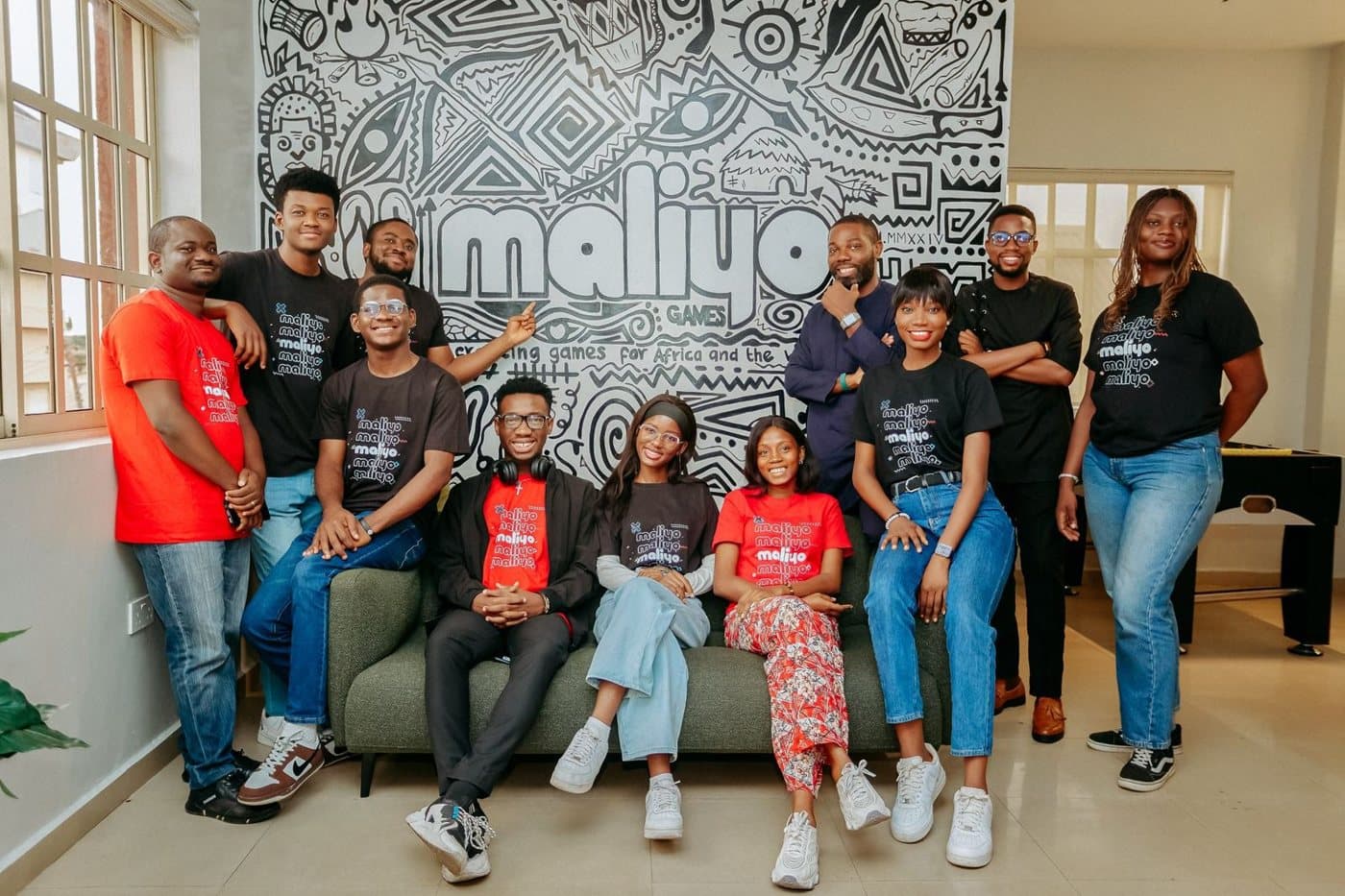 The Maliyo team gathered on sofas in front of the Maliyo wall mural